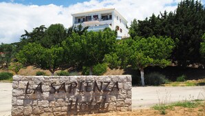 Une enseigne en pierre sur laquelle on peut lire « LAS SPENZA Hotel », un bâtiment blanc doté de balcons, entouré d’arbres.