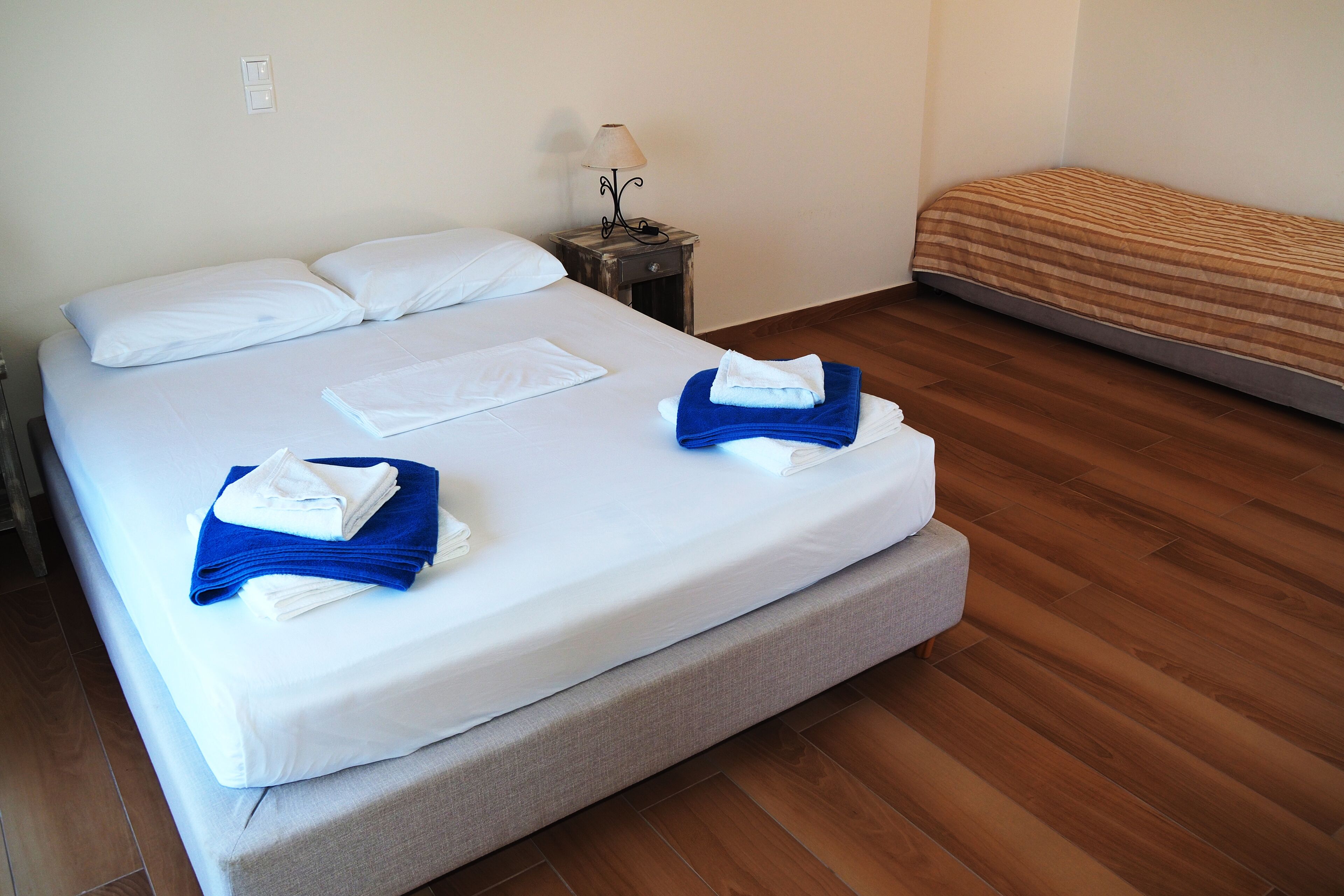 Un lit bien fait, avec des serviettes blanches et bleues, une table de chevet avec une lampe et un plancher en bois.