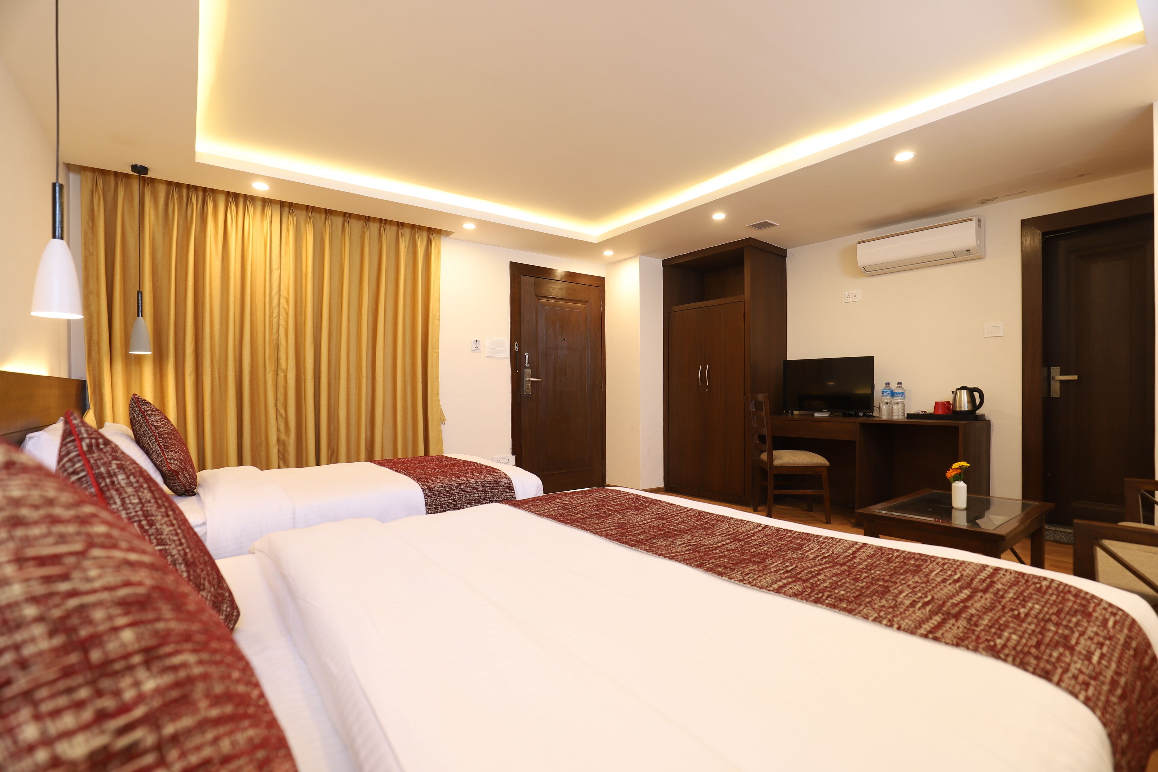 Quarto de hotel com duas camas, uma escrivaninha, uma cadeira, uma televisão e um ar condicionado.
