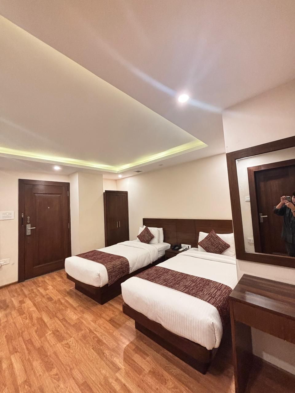 Habitación de hotel con dos camas, suelo de madera, un armario de madera, una mesita de noche y un espejo.