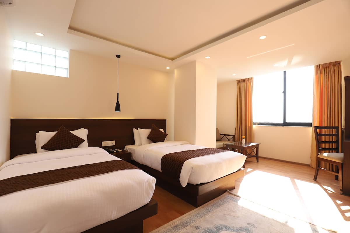 A hotel room with two beds, a desk, a chair, and a window with curtains.