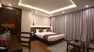 A modern hotel room with a large bed, wooden furniture, a glass coffee table, and a view of the city through curtains.