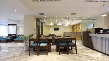 A modern hotel lobby with a marble floor, wooden furniture, a reception desk, and a seating area with sofas and a TV.