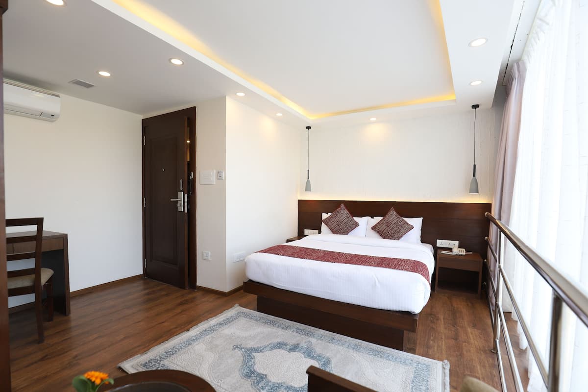 A hotel room with a wooden bed, a nightstand, a desk, and a chair.