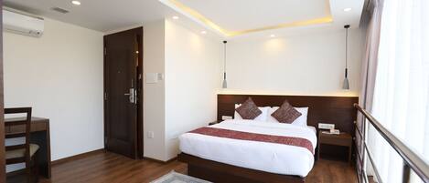 A hotel room with a wooden bed, a nightstand, a desk, and a chair.