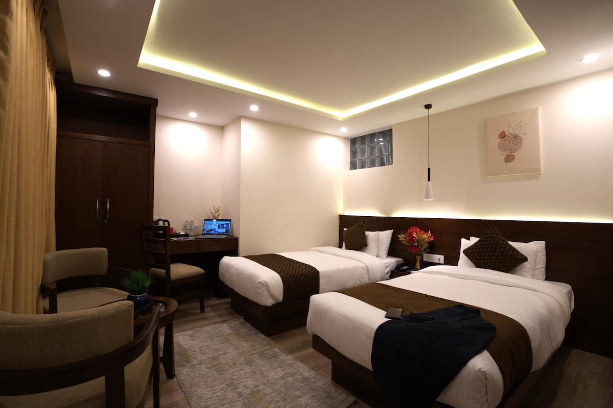 A hotel room with two beds, a desk with a computer, a chair, and a small table with a plant.