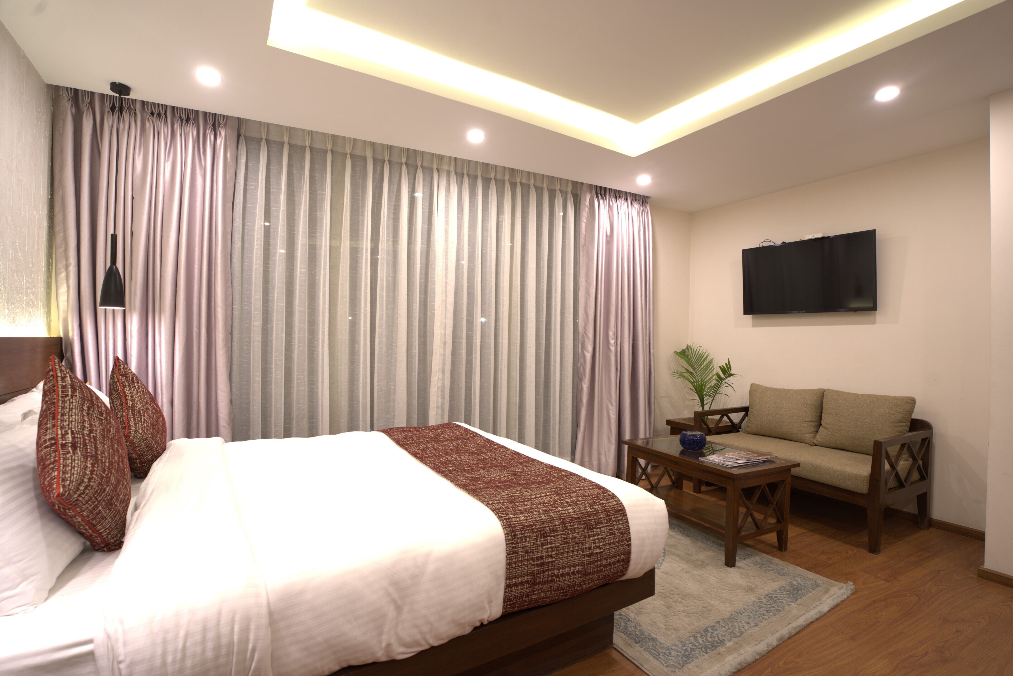 A modern hotel room with a large bed, a sofa, a flat-screen TV, and a small table.