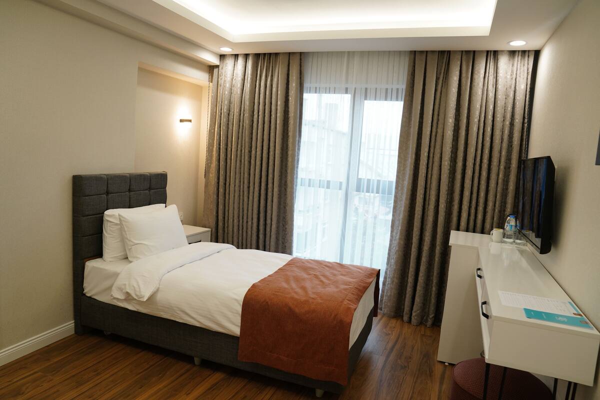 A hotel room with a bed, a desk, a chair, a television, and a window with curtains.