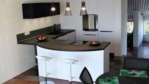 A modern kitchen with a central island, white bar stools, and pendant lighting. - Beautiful apartment near Brittany (Mandelieu-la-Napoule)