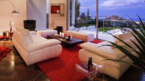 A modern living room with white sofas, a red rug, and a large window offering a view of the sea and hills. - Beautiful apartment near Brittany (Mandelieu-la-Napoule)