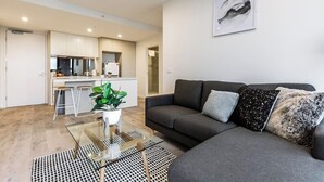 A modern living room with a grey sofa, a glass coffee table, and a potted plant.