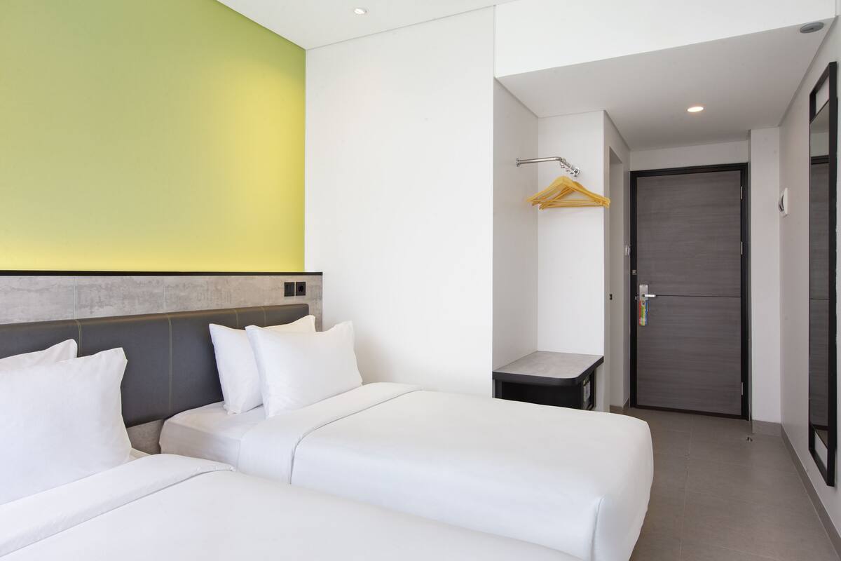 A hotel room with two beds, a small table, a coat rack, and a door.