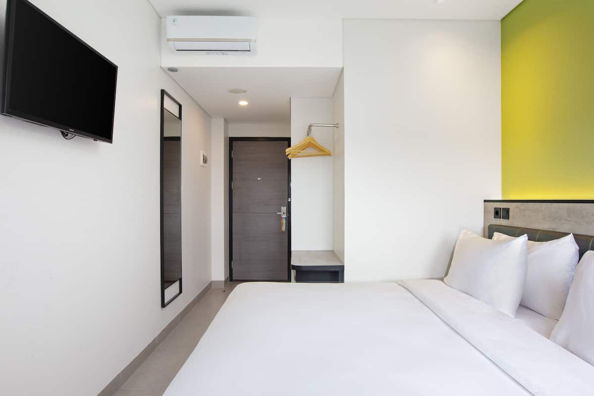 A hotel room with a bed, a TV mounted on the wall, a door, and a small bench.