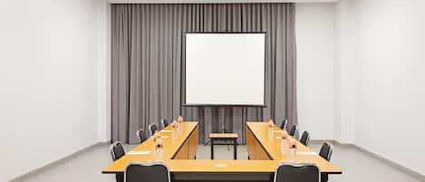 Una sala de conferencias con una mesa larga, sillas, una pantalla de proyector y un telón de fondo gris.