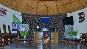A reception area with a stone wall, wooden chairs, a reception desk, and a television mounted on the wall. - Mora Heights Hotel (Arba Minch)