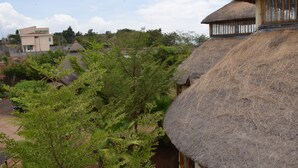 A traditional thatched-roof house with a wooden window frame, surrounded by lush greenery and other buildings in the background. - Mora Heights Hotel (Arba Minch)