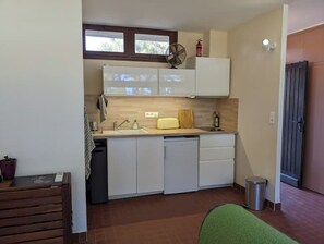 Eine kompakte Küche mit weißen Schränken, einem Spülbecken, einem Ventilator und einer kleinen Mülltonne.