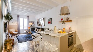 A modern kitchen with a central island, white cabinetry, and a built-in oven. There is a dining area with a sofa and a small table, and a living room with a sofa and a coffee table. - CASA COSTA 4 BEDROOM APT (Barcelona)