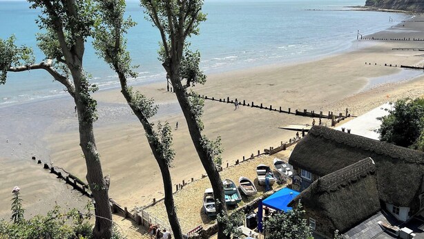 A beach with boats, a thatched-roof building, and a view of the sea. - Cherry Lodge (Godshill)