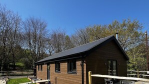 A small wooden cabin with a sloped roof, a fenced patio area, and a clear blue sky in the background. - Cherry Lodge (Godshill)