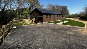 A small, single-story building with a dark roof and a gravel driveway leading to a wooden gate. - Cherry Lodge (Godshill)