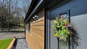 A modern building with wooden siding and a large window with a flower arrangement. - Cherry Lodge (Godshill)