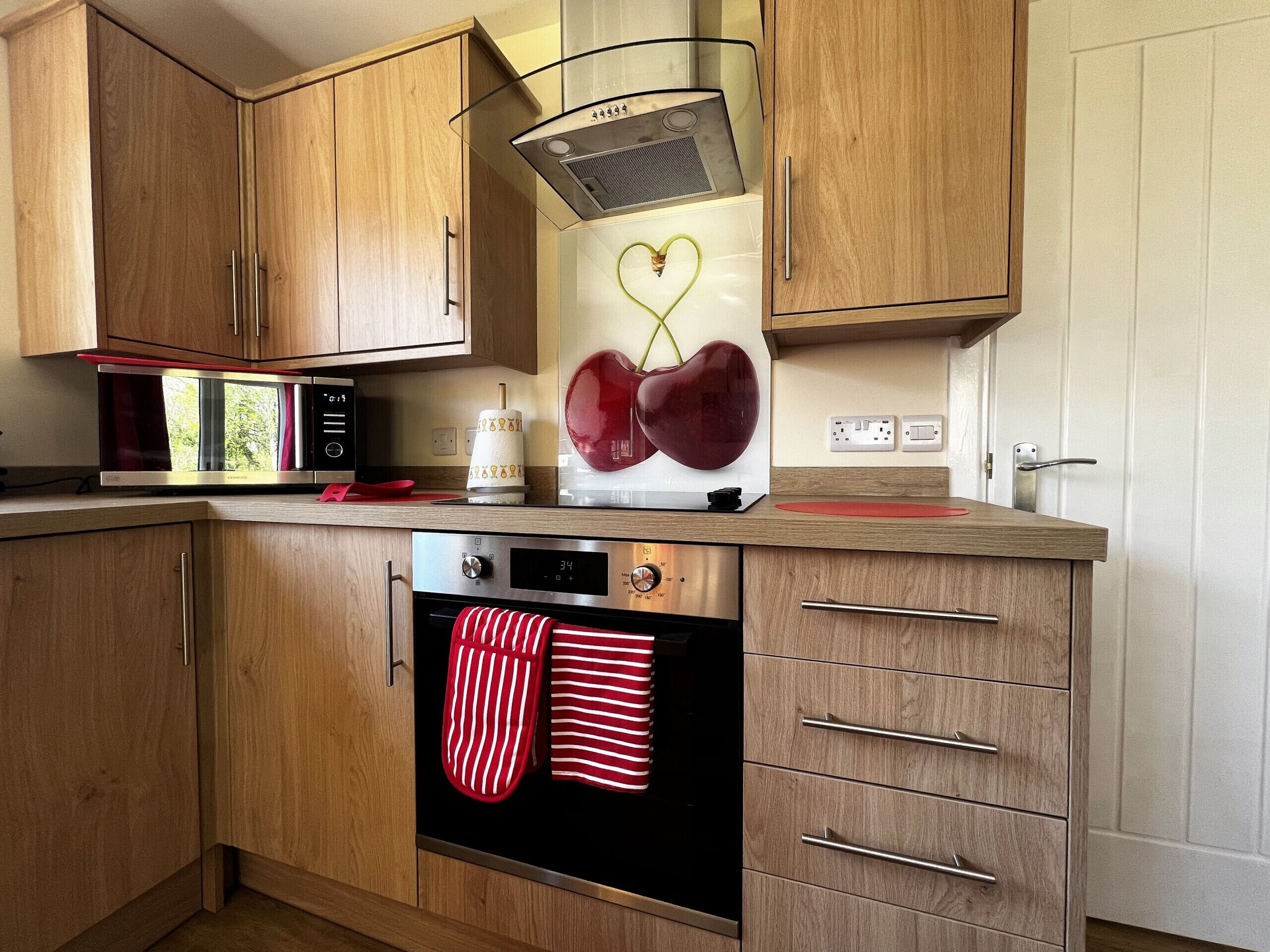 Una cocina con armarios de madera, microondas, horno empotrado y una decoración con forma de corazón en la pared.