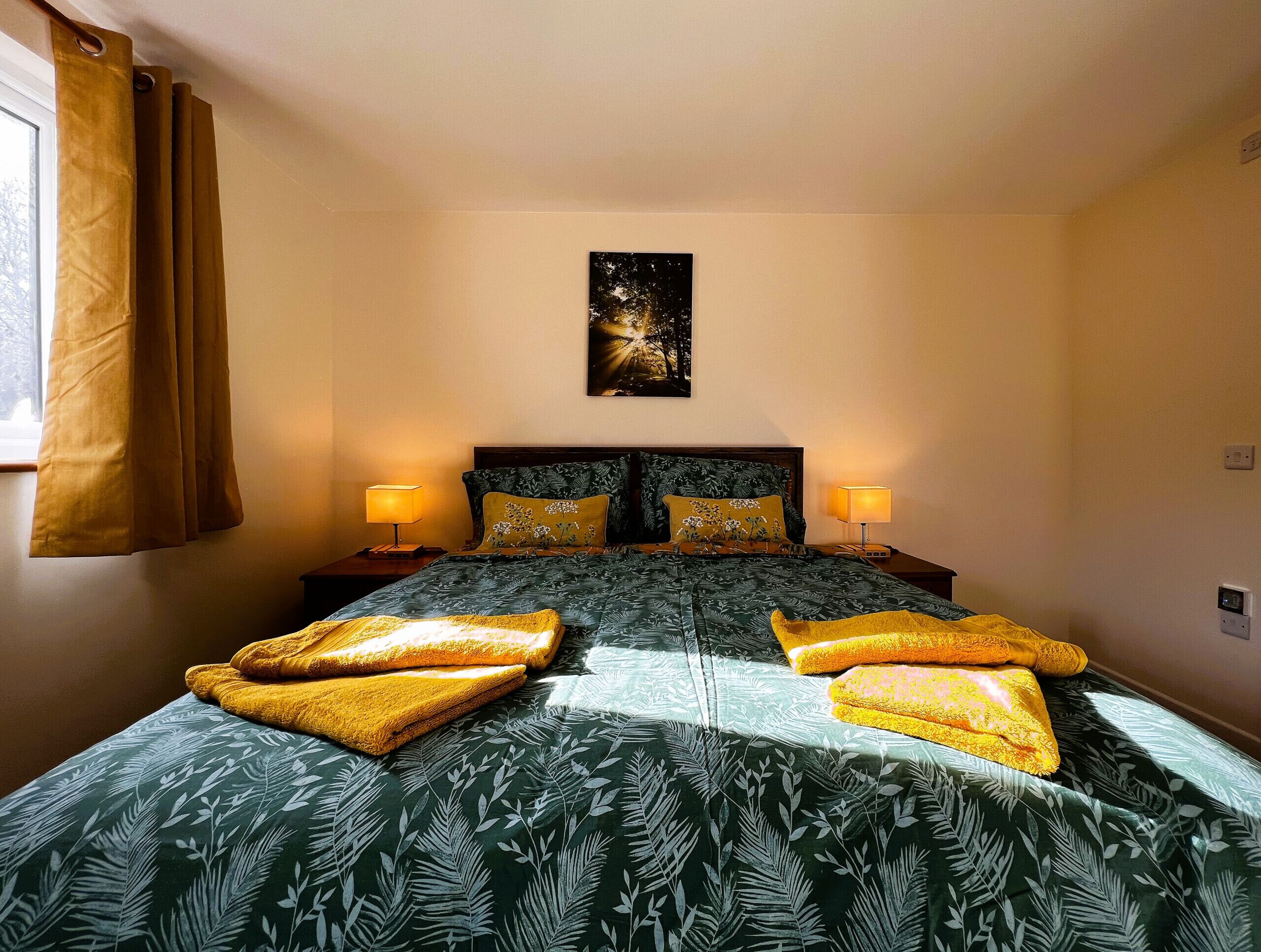 Una cama bien hecha con ropa de cama de estampado floral, dos lámparas de noche y un cuadro con un cielo estrellado en la pared.