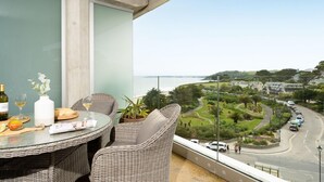 Un balcon agrémenté de meubles en osier, une table avec de la nourriture et des boissons, et une vue sur une route côtière et la verdure.