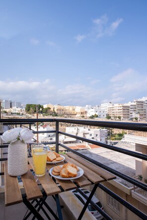 Un balcon avec une table dressée pour le petit-déjeuner, offrant une vue sur le paysage urbain.