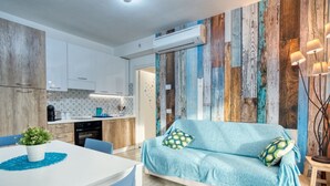 A modern kitchen with white cabinets, a dining table with blue chairs, and a blue sofa with patterned cushions.