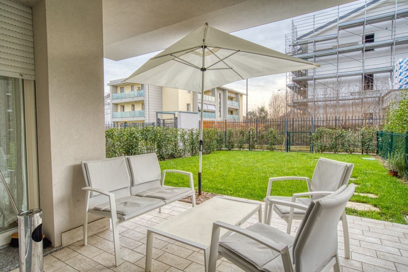 An outdoor patio with a table and chairs, a large umbrella, and a view of a residential building with scaffolding.