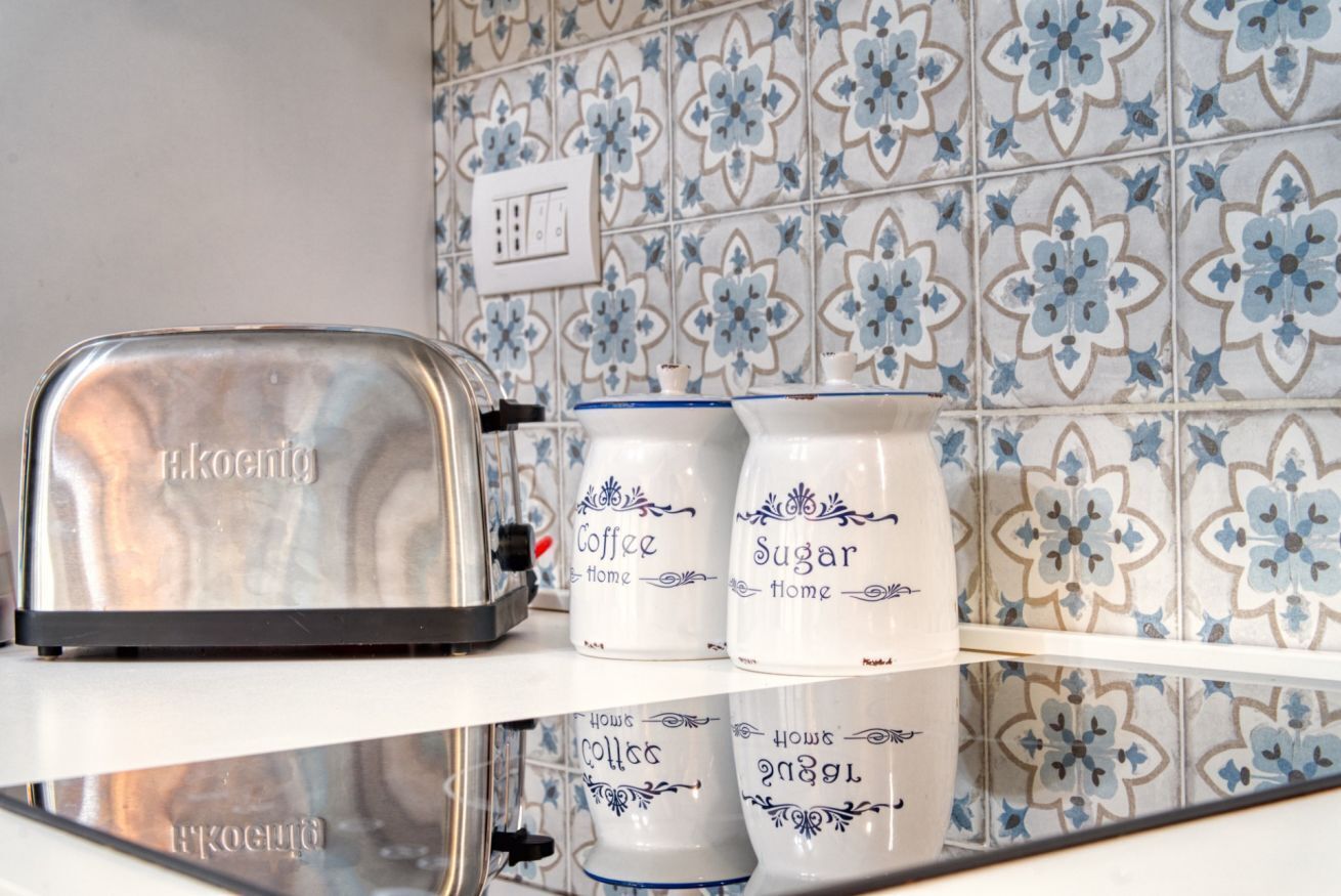 A kitchen with a toaster, two containers labeled 'Coffee Home' and 'Sugar Home,' and a patterned tile backsplash.