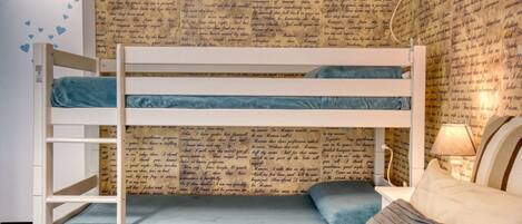 Una cama litera con un colchón azul, una mesita de noche con una lámpara, y una pared con texto impreso.