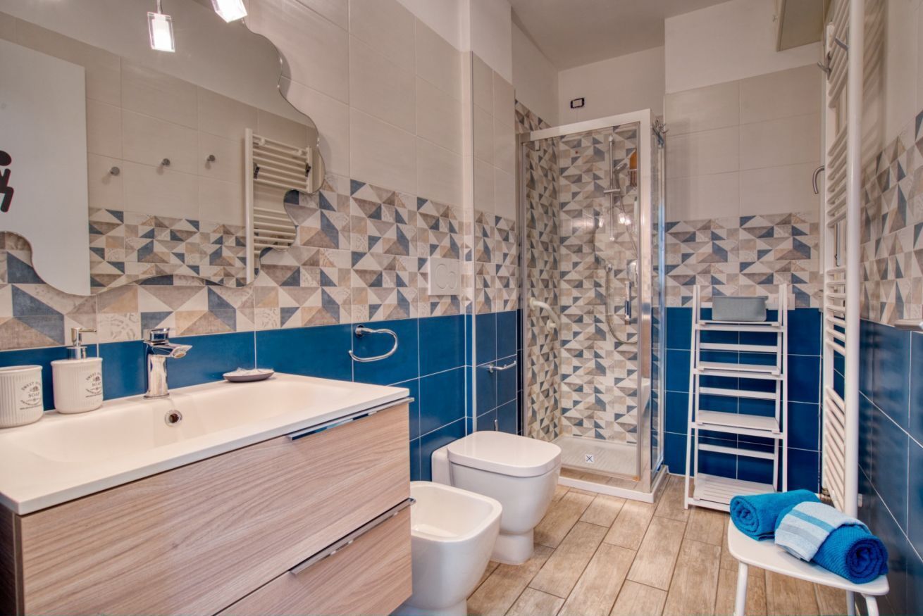 A bathroom with a sink, two toilets, a shower, and a towel rack.