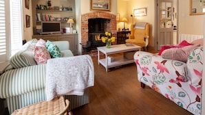 A cozy living room with a fireplace, striped sofas, a television, and a bookshelf. - Bluebell Cottage - sleeps 3 guests  in 2 bedrooms (Burnham Market)