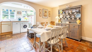 A kitchen with a dining table set for four, a washing machine, and a cabinet with dishes. - Bluebell Cottage - sleeps 3 guests  in 2 bedrooms (Burnham Market)
