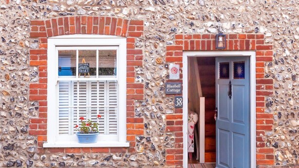 A cottage with a stone facade, a window with shutters, and a door with a sign reading "Bluebell Cottage." - Bluebell Cottage - sleeps 3 guests  in 2 bedrooms (Burnham Market)
