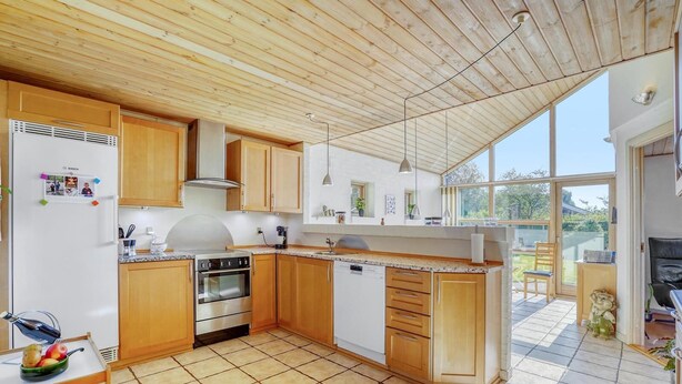 A modern kitchen with wooden cabinets, a built-in oven, and a dishwasher. - Lækkert hus tæt på alt (Billund)