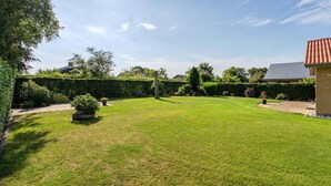 A well-maintained lawn with a hedge, a small tree, and a brick building with a red roof. - Lækkert hus tæt på alt (Billund)