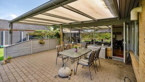 An outdoor patio with a covered seating area, a barbecue grill, and a table with chairs. - Lækkert hus tæt på alt (Billund)