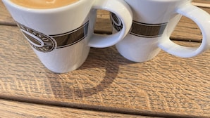 Two white coffee cups with heart-shaped latte art on a wooden table. - Lækkert hus tæt på alt (Billund)