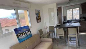 Una sala de estar con un sofá color crema, una mesa de comedor con sillas y una cocina con ventana.