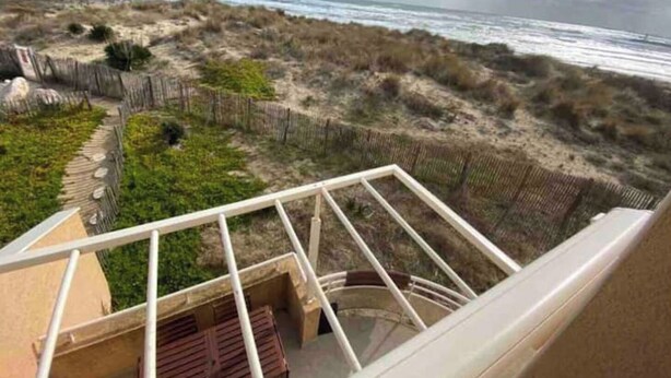Vista desde un balcón sobre una playa con arena y una valla de madera.