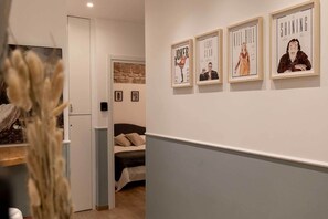 Un pasillo con una cama, una puerta y carteles de películas enmarcados en la pared.
