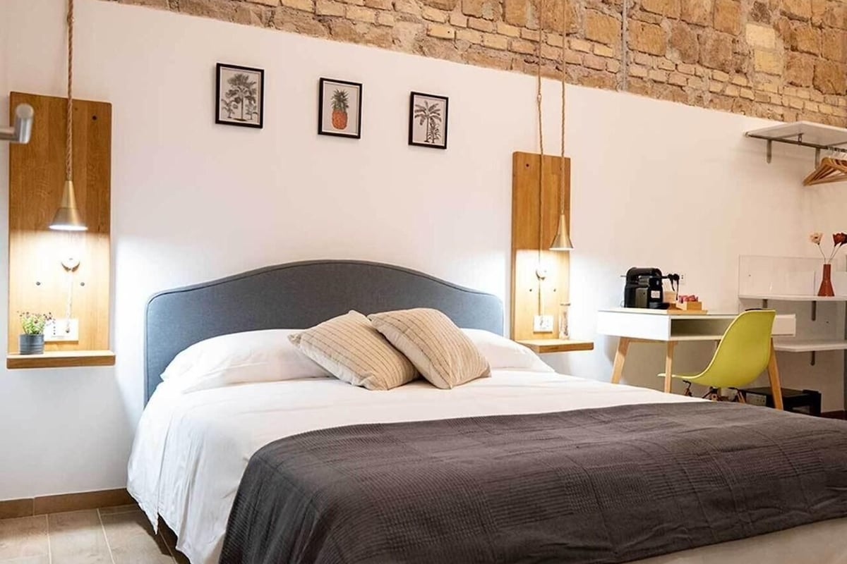 A bedroom with a bed, a desk, and a chair. There are three framed pictures on the wall.