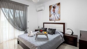 A bedroom with a bed, a bedside table, a nightstand, a painting, and a window with curtains. - Amazing Summer Villa in Kolympia (Κολύμπια)
