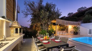 An outdoor dining area with a pool, a grill, and a seating arrangement. - Amazing Summer Villa in Kolympia (Κολύμπια)