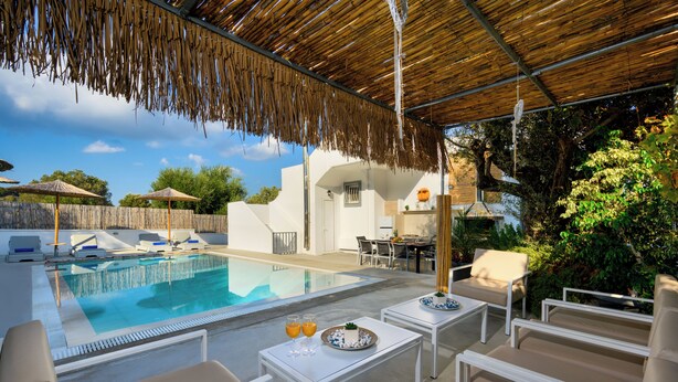 A pool area with lounge chairs, a table with drinks, and a covered seating area. - Amazing Summer Villa in Kolympia (Κολύμπια)