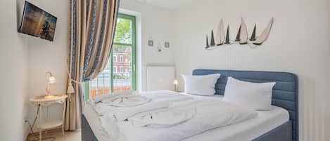 A neatly made bed with white linens, a blue headboard, and a wall-mounted TV.